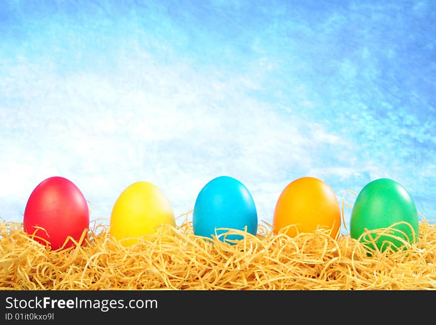 Five painted eggs on a straw on a clear sky background