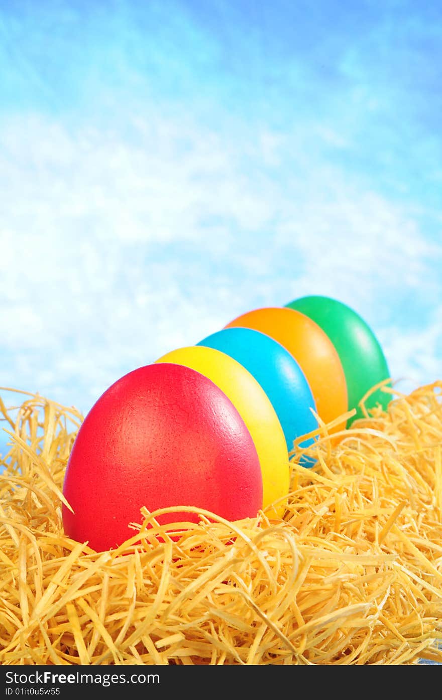 Five painted eggs in straw on a sky background