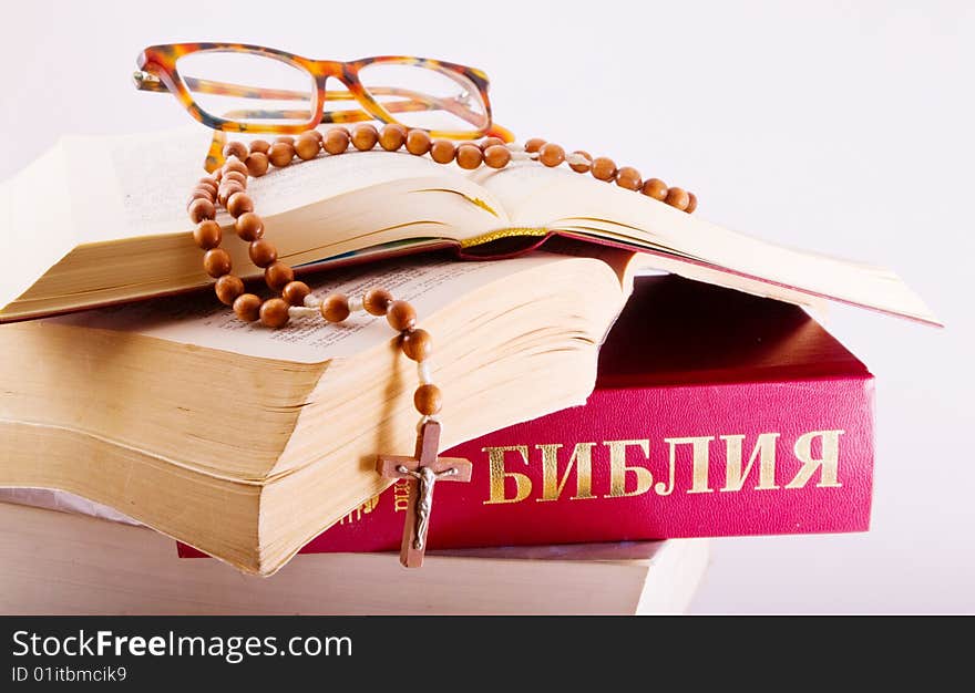 Open Holy Bible lying on stack of old books with glasses, cross and beads. Open Holy Bible lying on stack of old books with glasses, cross and beads