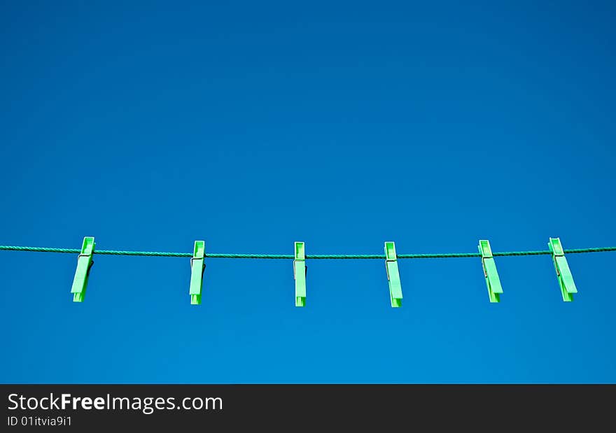 Green clothes pegs on a washing line against a blue sky background.