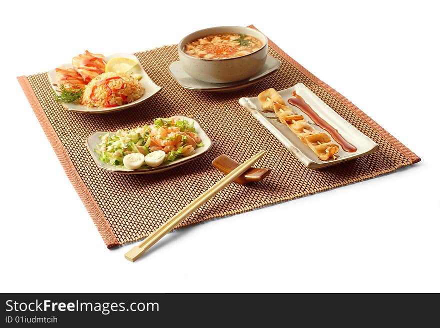 Asian lunch with salmon teriyaki, rice with vegetables, sake dzosuy, yakitori ika and chopsticks on the matting over white background. Asian lunch with salmon teriyaki, rice with vegetables, sake dzosuy, yakitori ika and chopsticks on the matting over white background