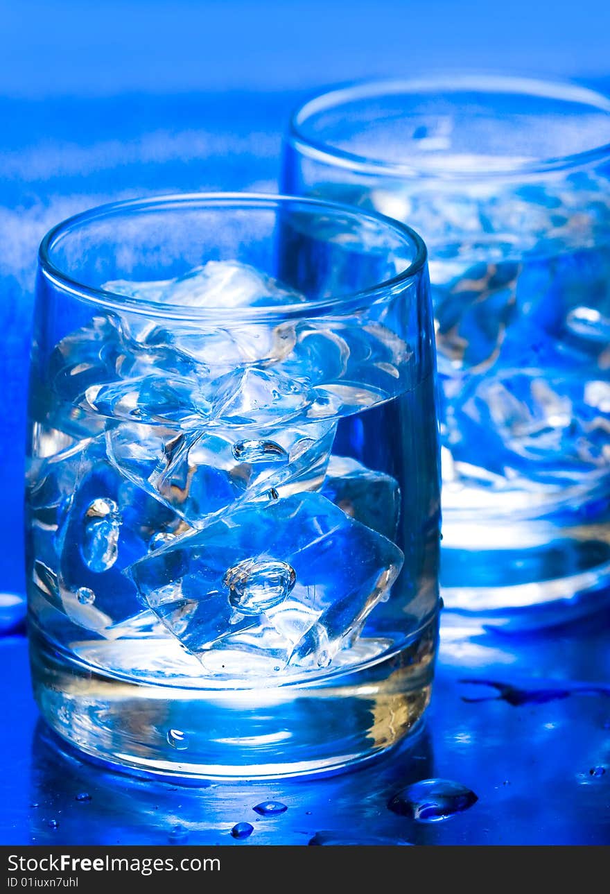 Glass with water and ice over blue