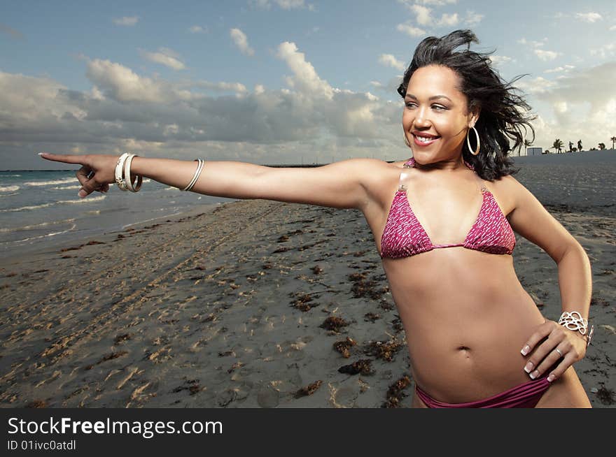 Young woman on the beach smiling and pointing towards the ocean