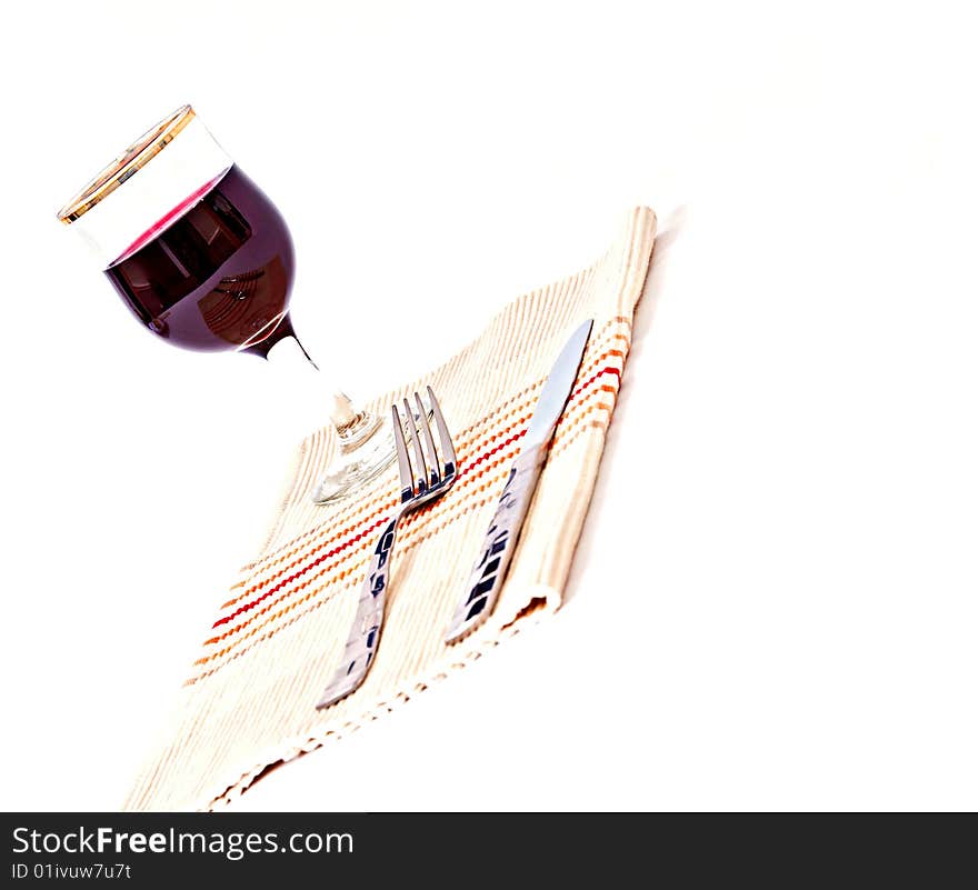 A trendy place setting isolated against a white background with a glass of red wine as the focal point.