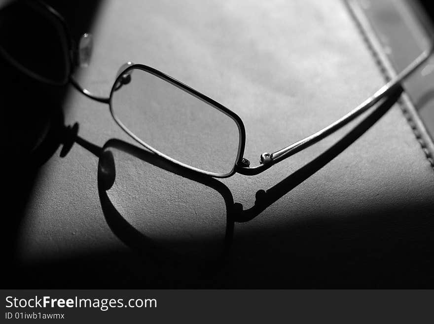 Pair of man's glasses on a leather business pad silhouetted against the sun. Sharp shadow on left hand side. Pair of man's glasses on a leather business pad silhouetted against the sun. Sharp shadow on left hand side