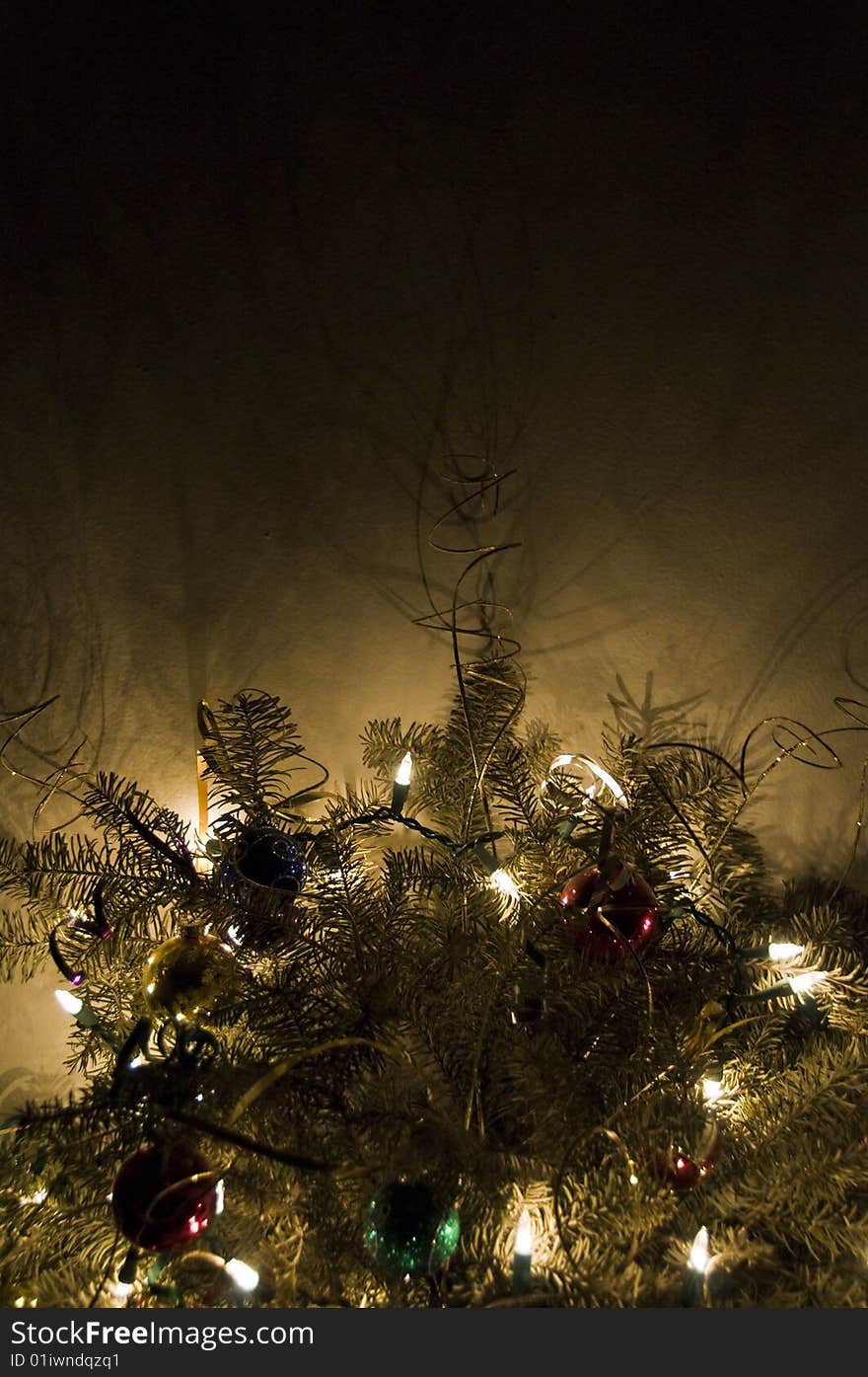 A pine bough decorated with Christmas ornaments and electric lights radiating a warm glow into darkness. A pine bough decorated with Christmas ornaments and electric lights radiating a warm glow into darkness