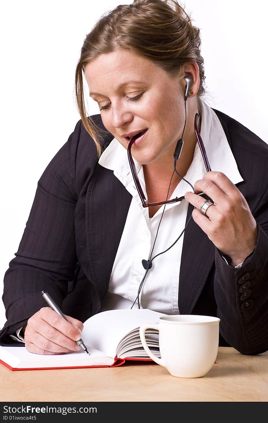 Modern woman writing in notebook with a satisfied expression and handsfree earplug. Modern woman writing in notebook with a satisfied expression and handsfree earplug.