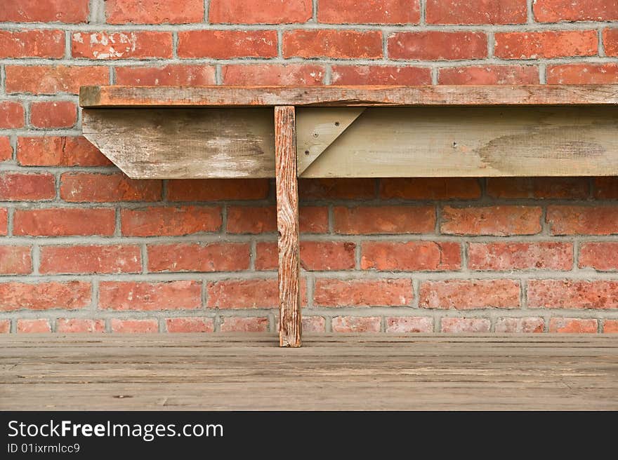 An old wooden bench against a red brick wall. An old wooden bench against a red brick wall