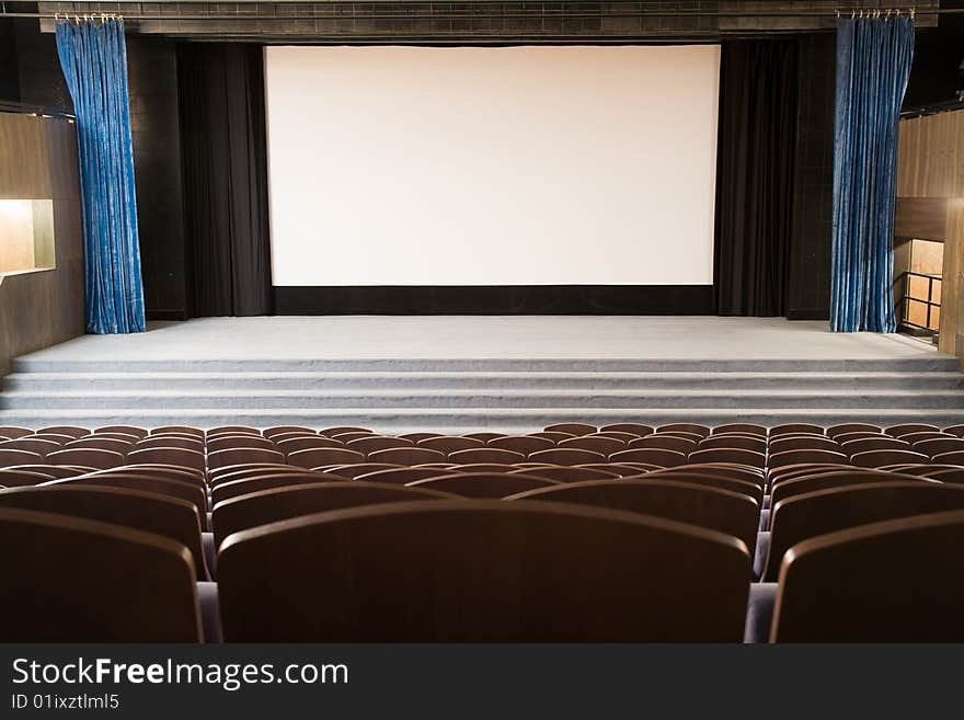 Empty cinema auditorium with line of chairs and stage with silver screen. Ready for adding your own picture. Empty cinema auditorium with line of chairs and stage with silver screen. Ready for adding your own picture.