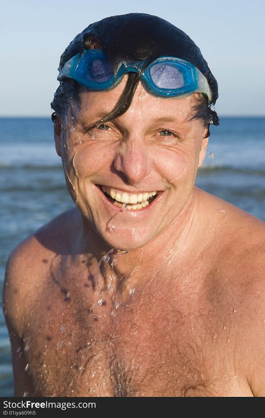 A portrait of a happy laughing forties man wearing swimming goggles with water dripping down his face. A portrait of a happy laughing forties man wearing swimming goggles with water dripping down his face.