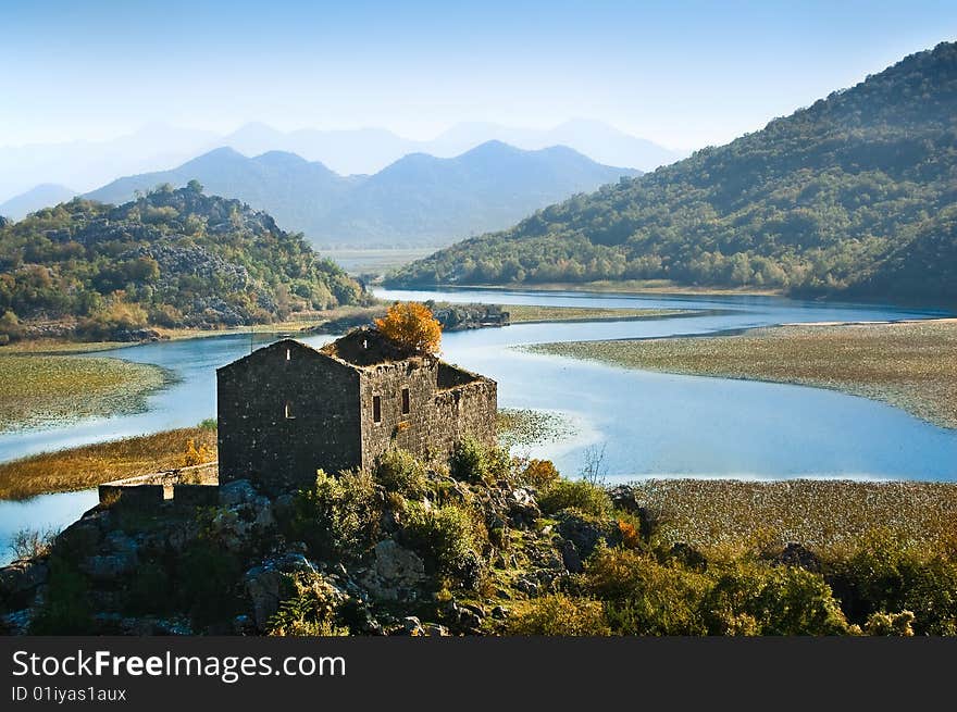 Ruined medieval castle and still river in Montenegro. Hills covered with woods and blue misty mountain range on the background. Ruined medieval castle and still river in Montenegro. Hills covered with woods and blue misty mountain range on the background