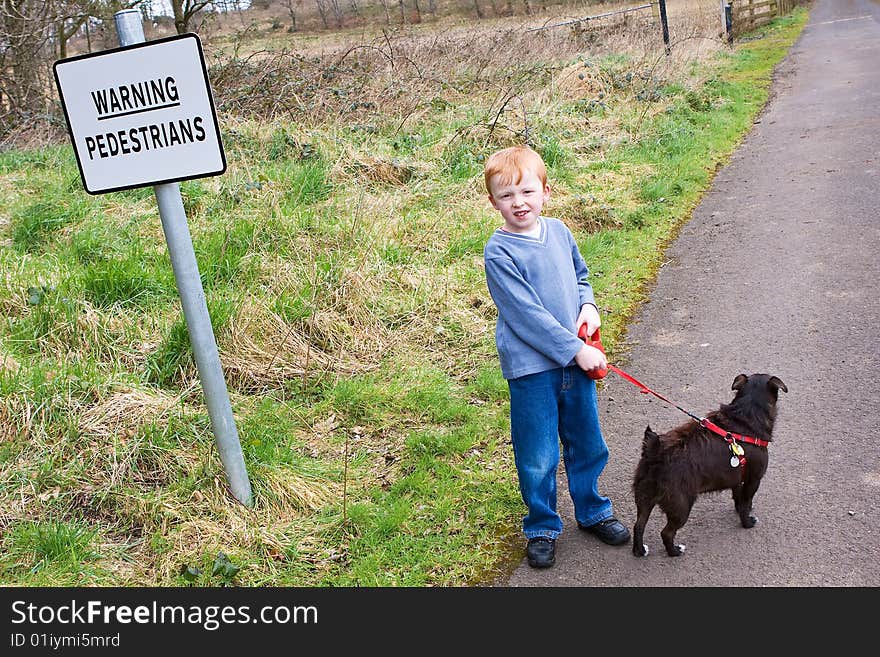 Young boy with his pet dog standing next to a sign that warns of pedestrians. Young boy with his pet dog standing next to a sign that warns of pedestrians