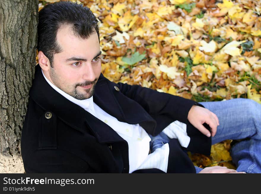 A man sits on the ground leaning the tree. A man sits on the ground leaning the tree