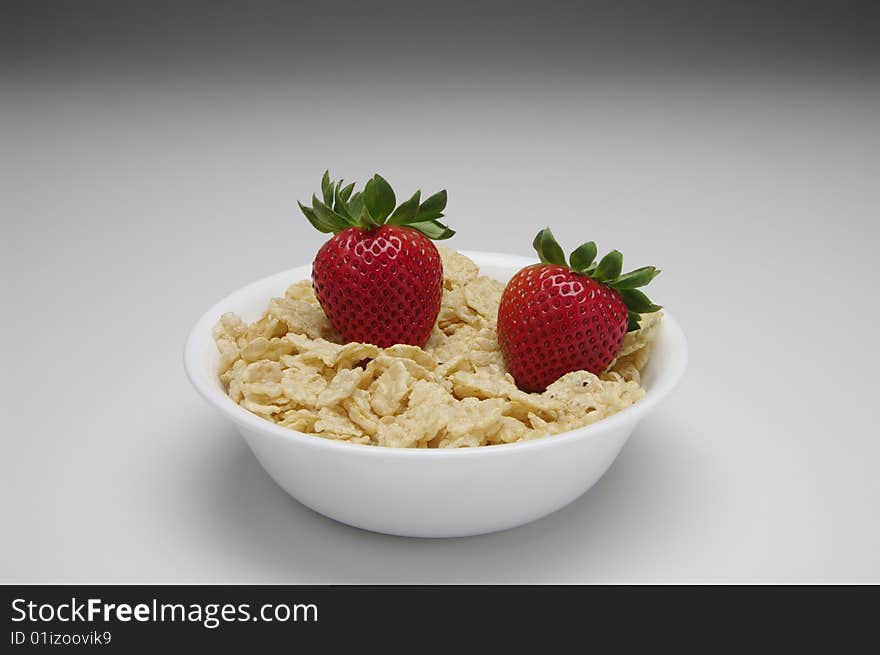 Red and green strawberries with cereal in a white bowl on a white background