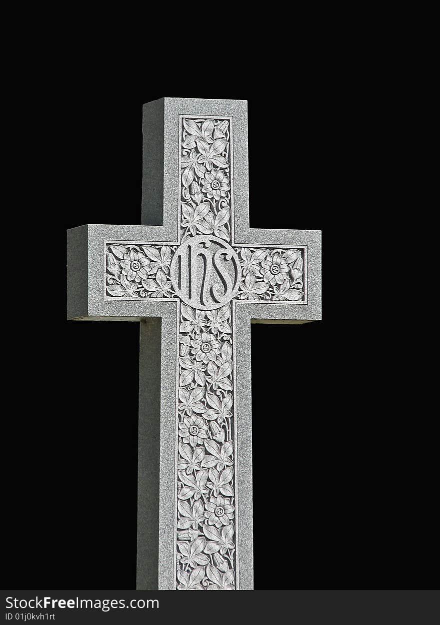 A granite cross (tombstone) with IHS inscription and floral carving on black background. A granite cross (tombstone) with IHS inscription and floral carving on black background.