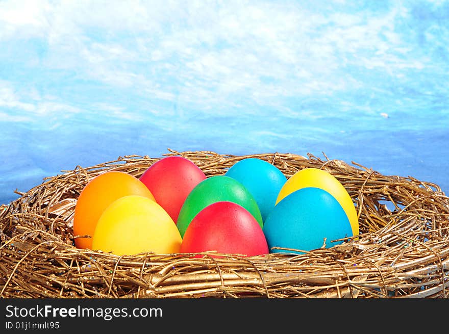 Color eggs in a golden nest on blue sky background