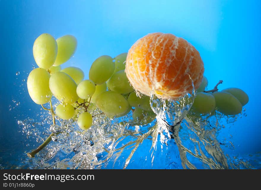 Orange and grapes in water, on a blue background. Orange and grapes in water, on a blue background