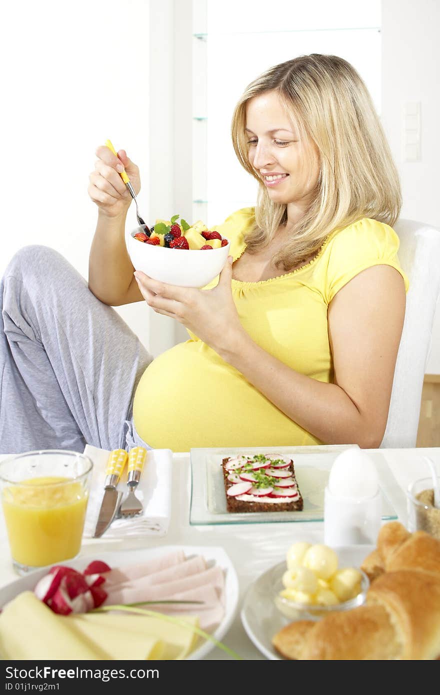 Beautiful young pregnant woman eats fruit salad