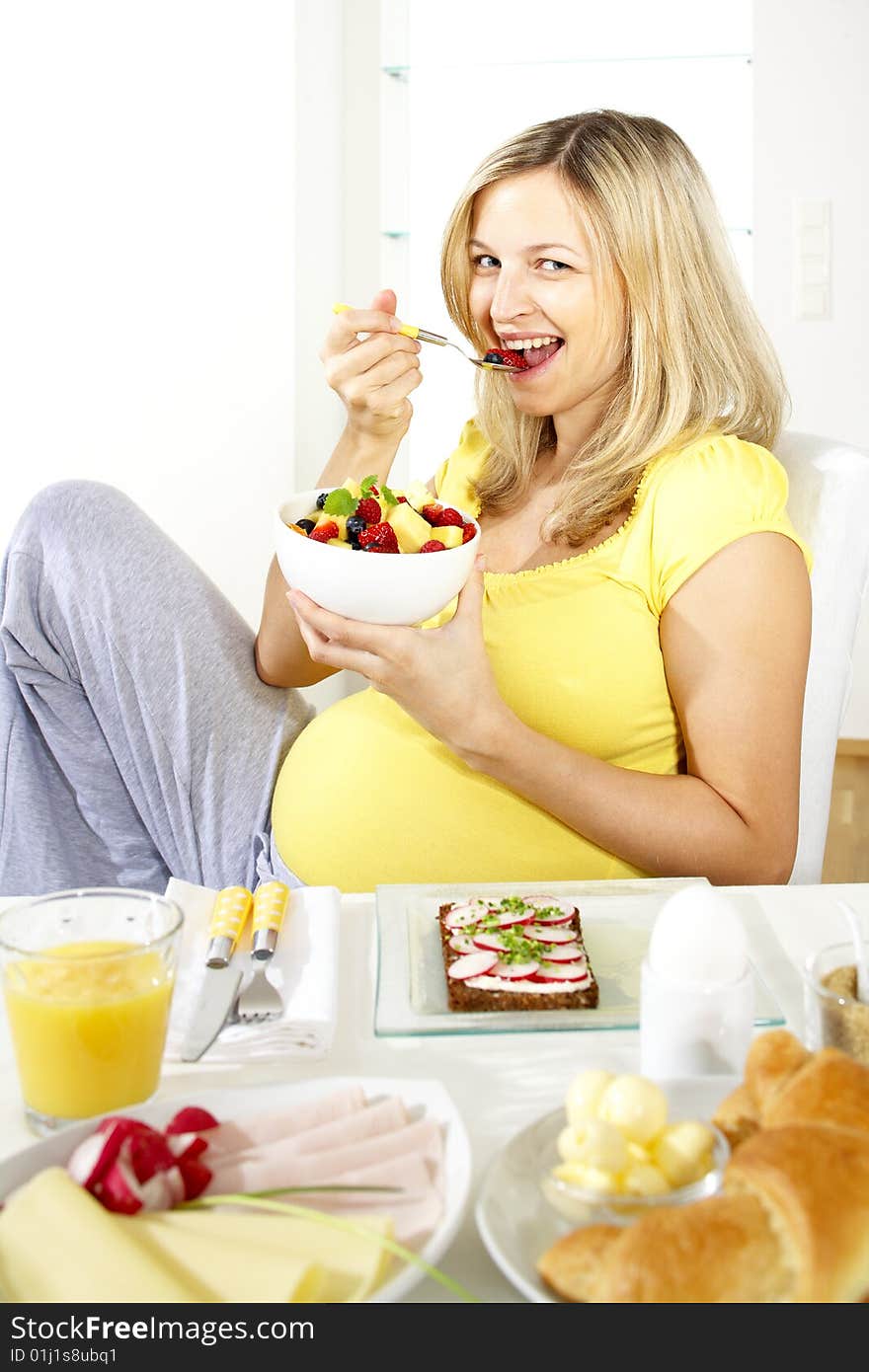 Beautiful young pregnant woman eats fruit salad