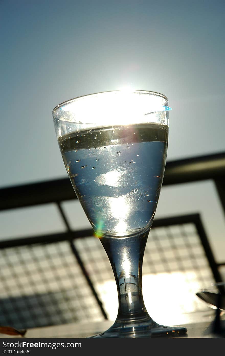 Close-up of a glass of water on balcony, sun reflects in the glass. Close-up of a glass of water on balcony, sun reflects in the glass.