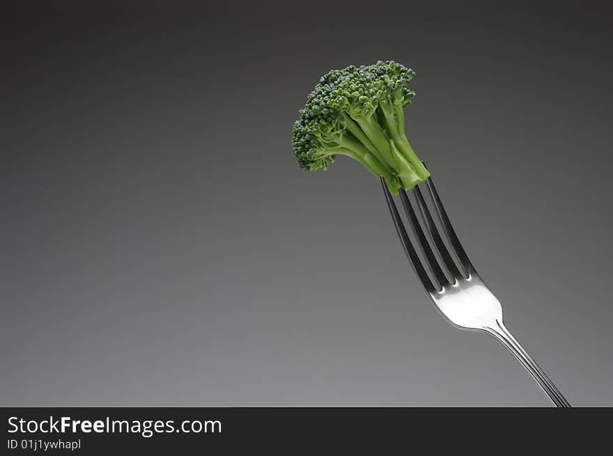 Broccoli stalk on a silver fork, on dark background, horizontal. Broccoli stalk on a silver fork, on dark background, horizontal.