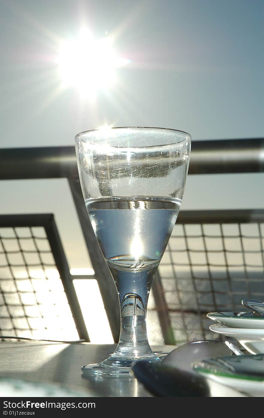 Glass of water on balcony, the sun is shining on the left.