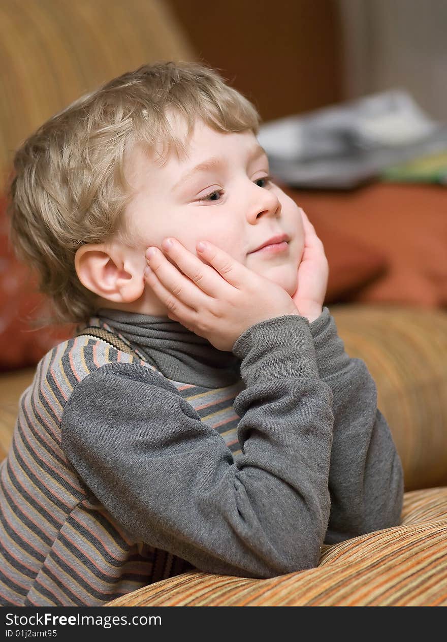 Cute little boy supporting his head with hands and looking at something