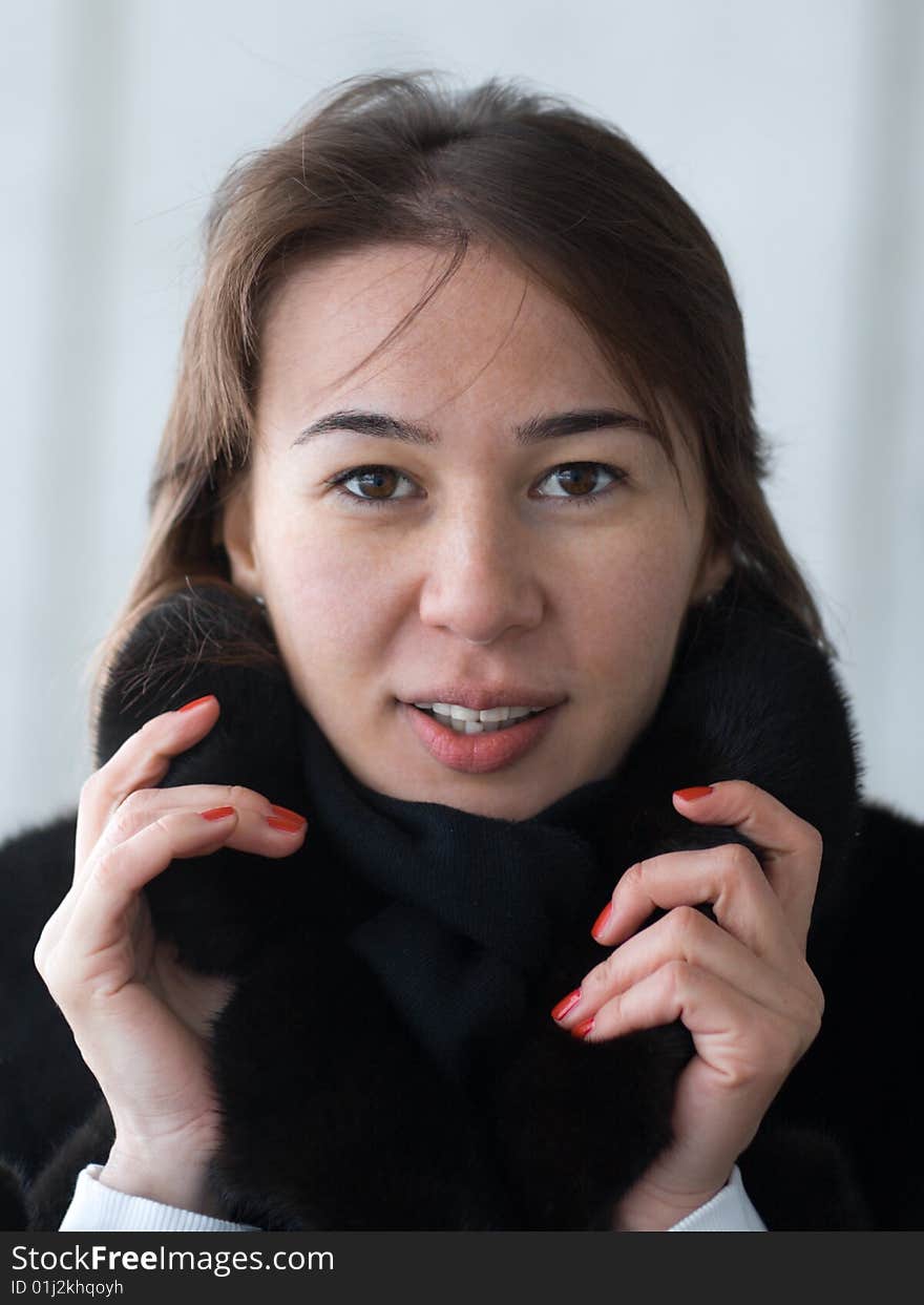 Pretty lady adjusting her fur coat' collar - portrait on gray background