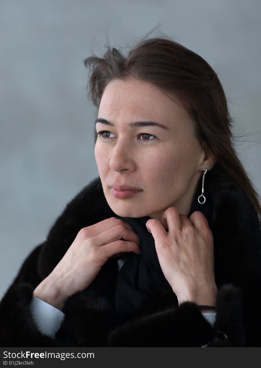 Pretty lady adjusting her fur coat' collar - portrait on gray background