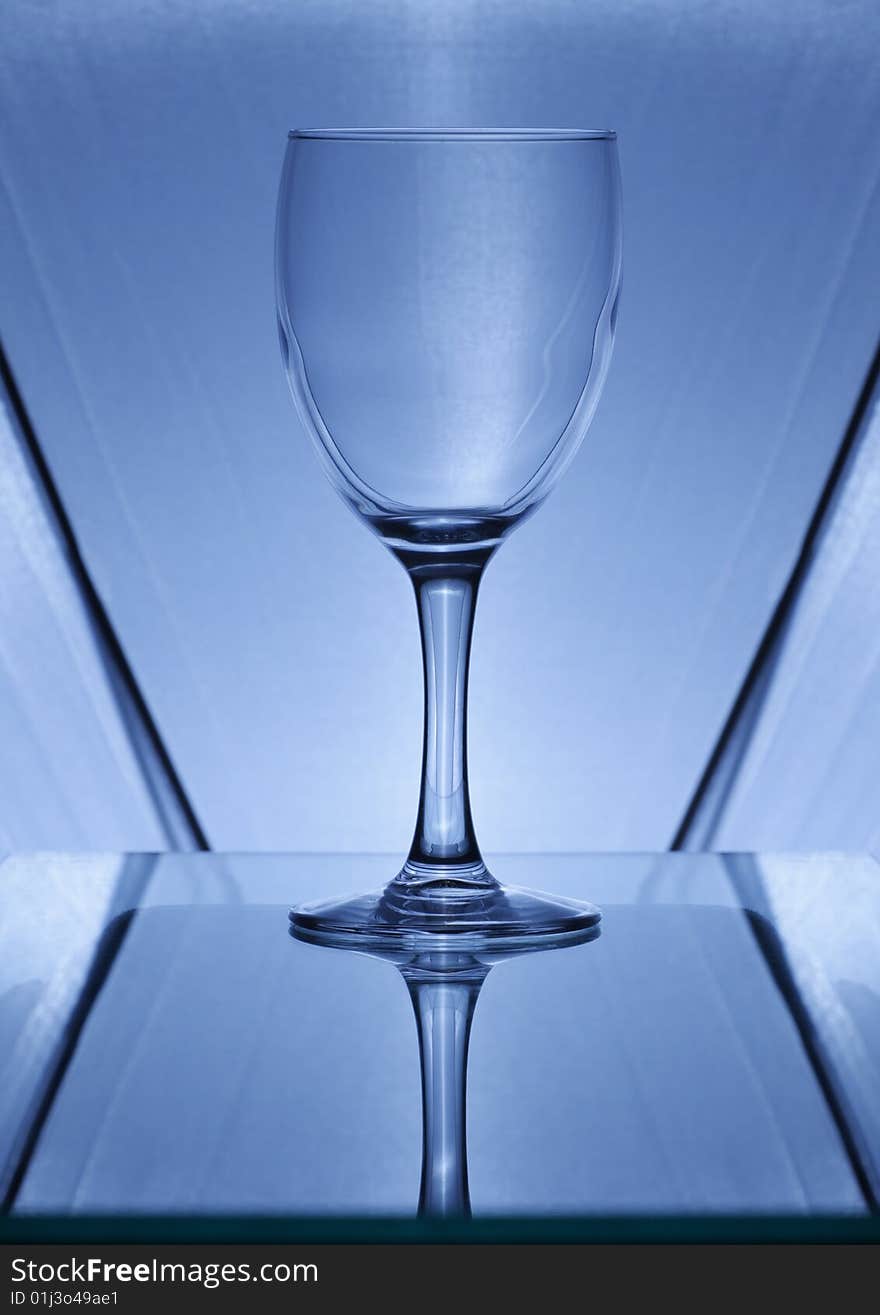 The blue wine glass whith reflection on a glass background. The blue wine glass whith reflection on a glass background