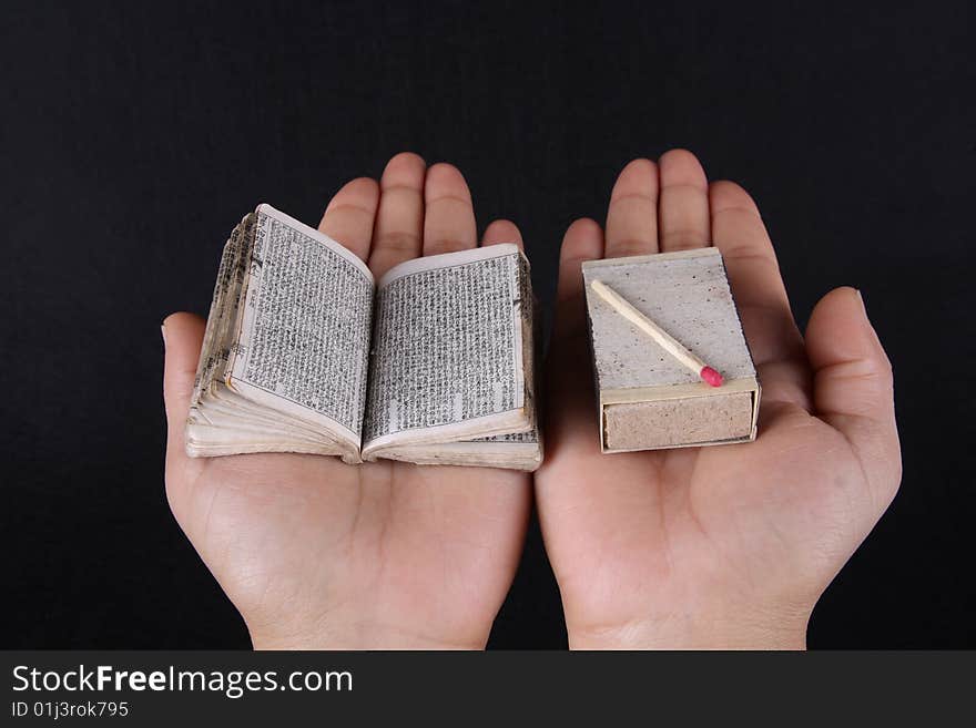 A mini book and matchbox contrast on hand over black background