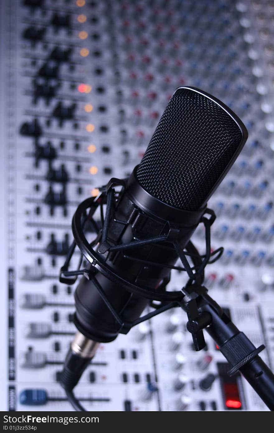 A black studio condenser mic in front of a sound board. A black studio condenser mic in front of a sound board.