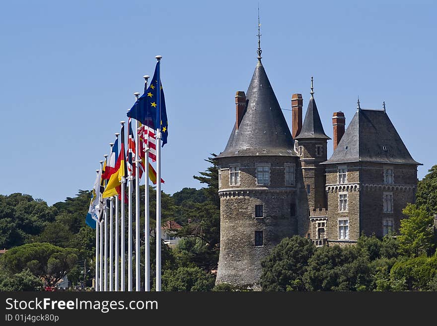 Ten flags on flag poles adjacent to a French chateau surrounded by trees, set against a blue summer sky. Horizontal Orientation. Ten flags on flag poles adjacent to a French chateau surrounded by trees, set against a blue summer sky. Horizontal Orientation