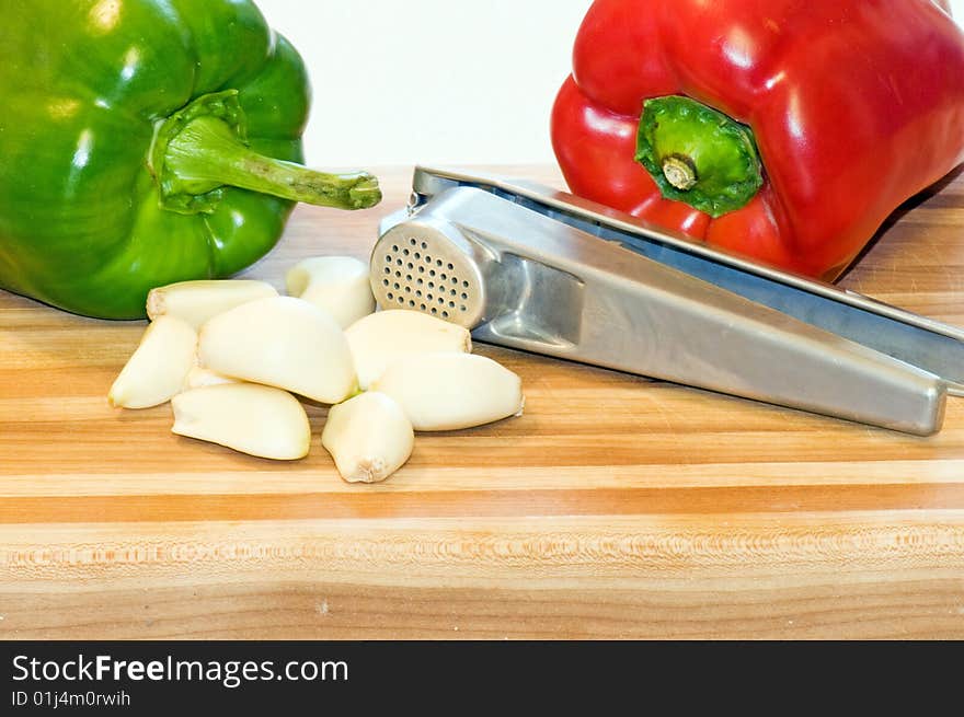 Whole red and green pepper on a wooden cutting board with garlic cloves and a garlic press. Whole red and green pepper on a wooden cutting board with garlic cloves and a garlic press.