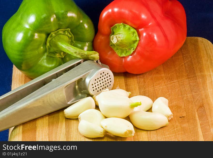 Whole red and green pepper on a wooden cutting board with garlic cloves and a garlic press. Whole red and green pepper on a wooden cutting board with garlic cloves and a garlic press.