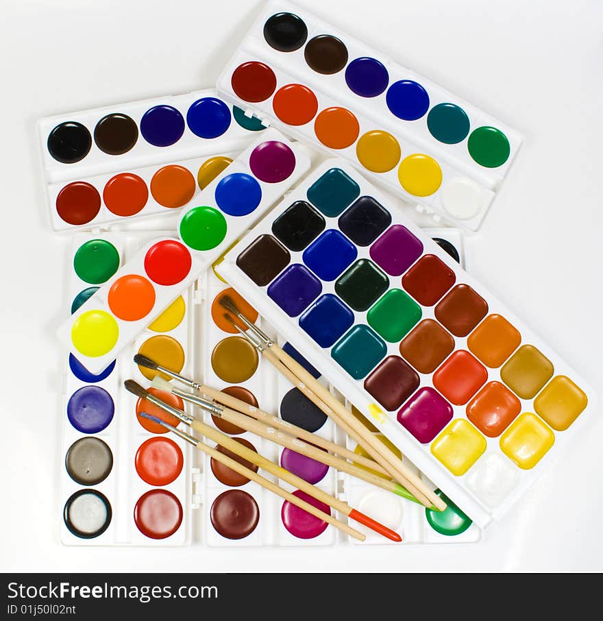 Some brushes on a background of water colour paints on white