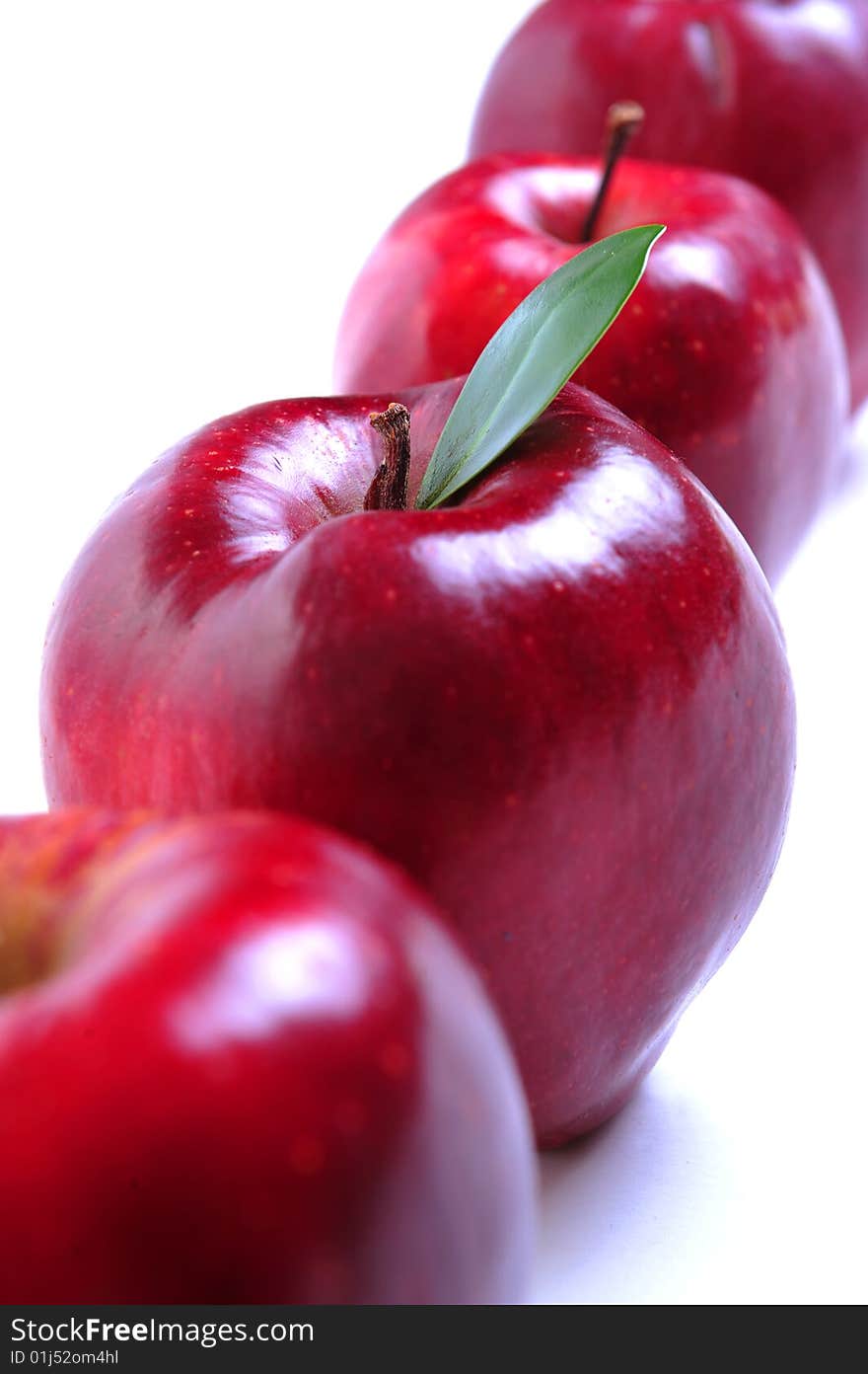 Row of four red apples on white background, selective focus on second apple