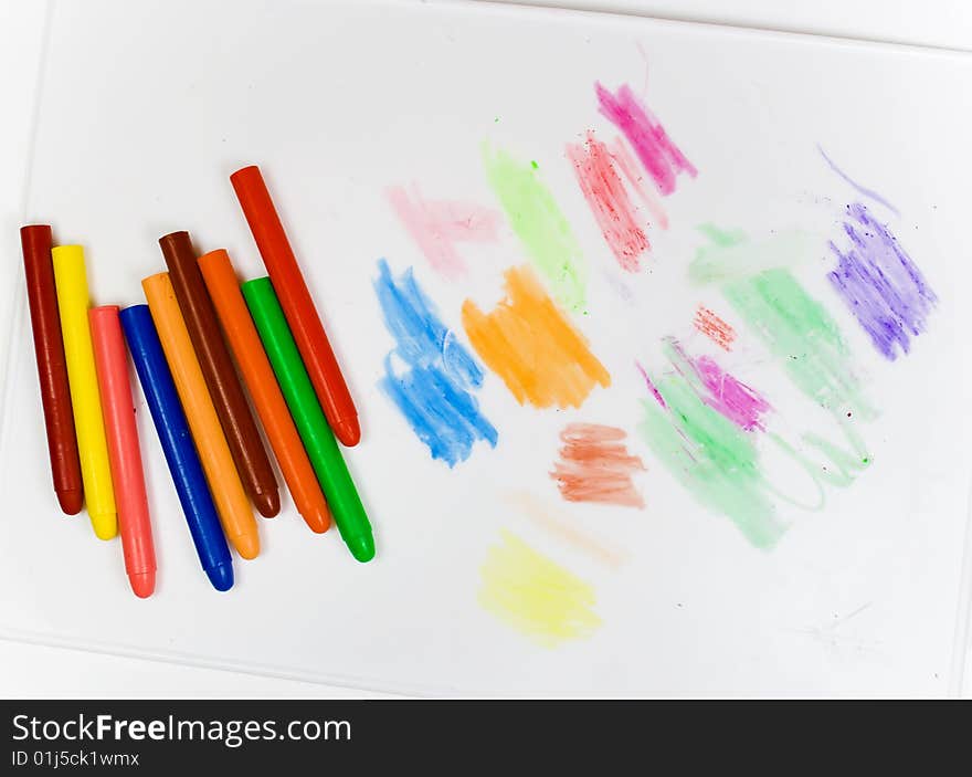 Eight oil pencils on a white plastic board with traces of drawing