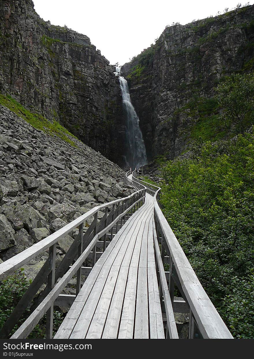 A wooden walkpath leading to a waterfall.