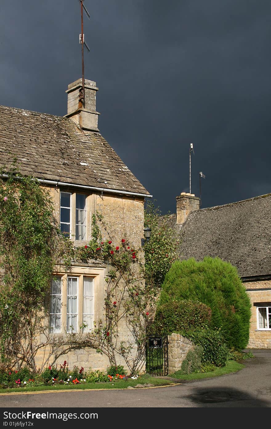 Cotswold house in sunshine with stormclouds approaching