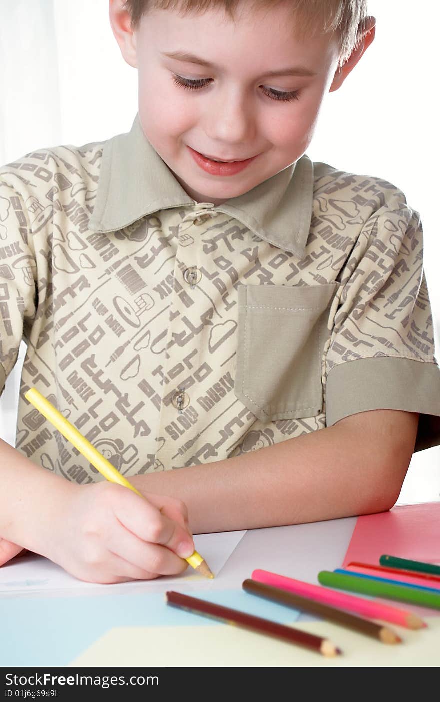 6 year old boy draws pencils sitting for a table. 6 year old boy draws pencils sitting for a table