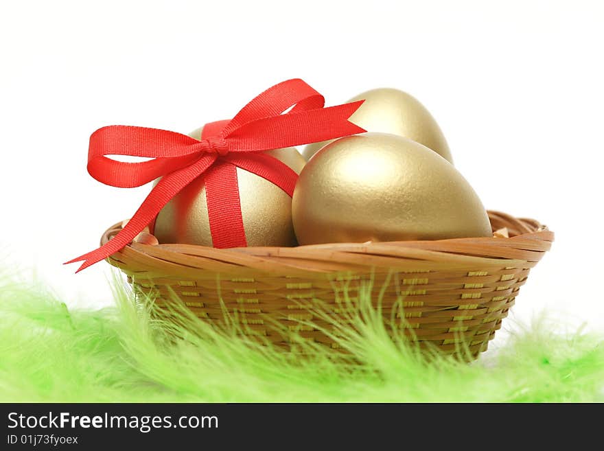 Golden egg wrapped around with red ribbon in basket on green feathers. Golden egg wrapped around with red ribbon in basket on green feathers.