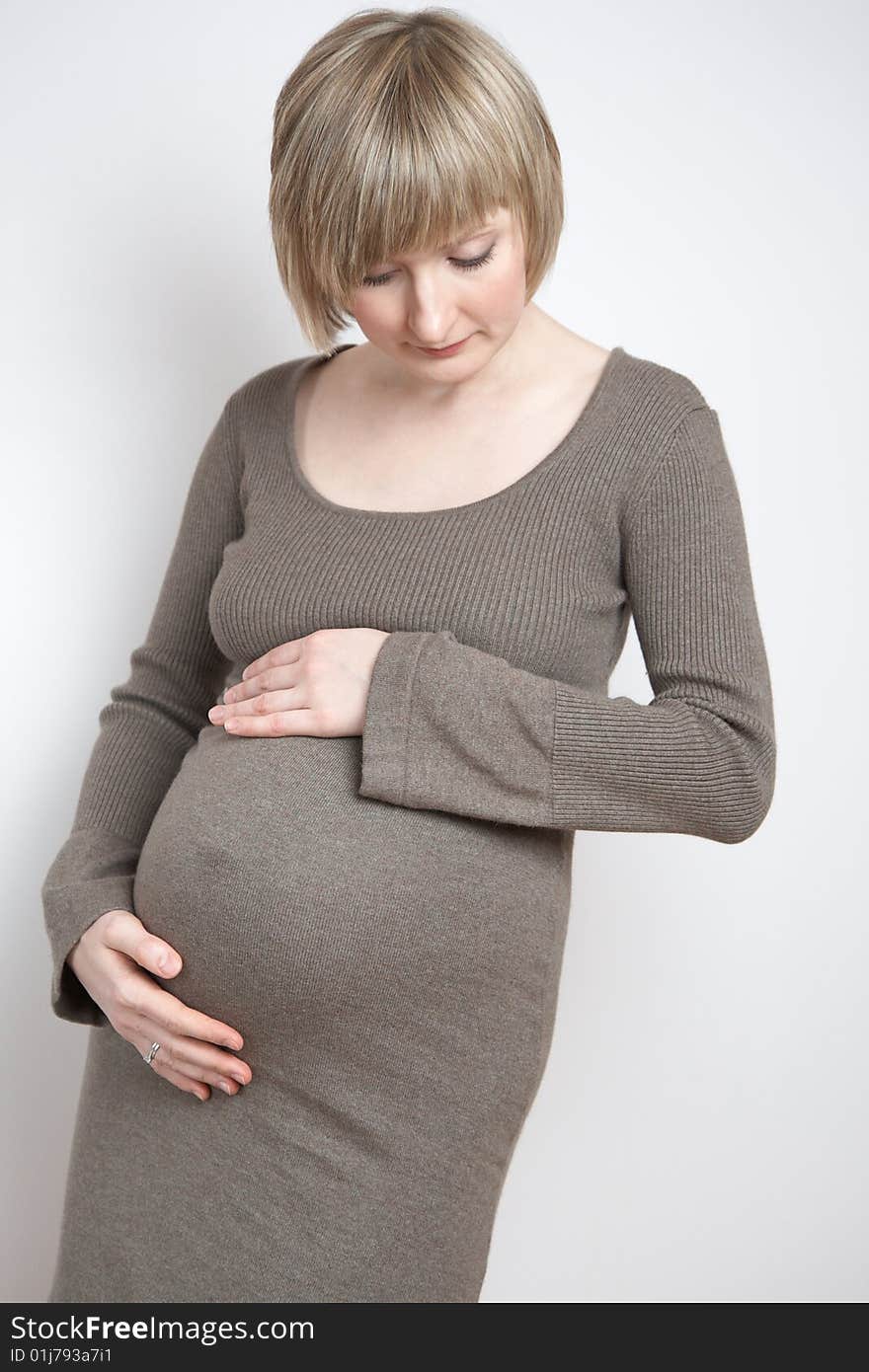 Full-body portrait of a pregnant woman in a dark beige dress