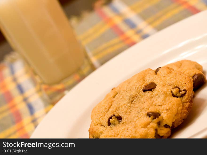 Chocolate chip cookies on a white plate in front of a glass of milk