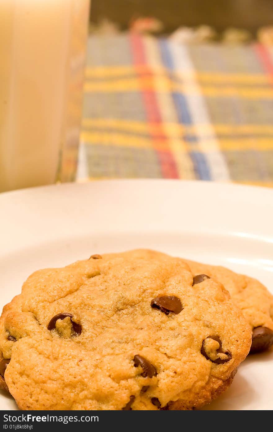 Chocolate chip cookies on a white plate in front of a glass of milk