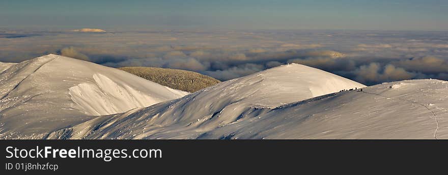 A group of mountaineers in winter are climbing in the Carpathian Mountains at sunset with clouds underneath. A group of mountaineers in winter are climbing in the Carpathian Mountains at sunset with clouds underneath