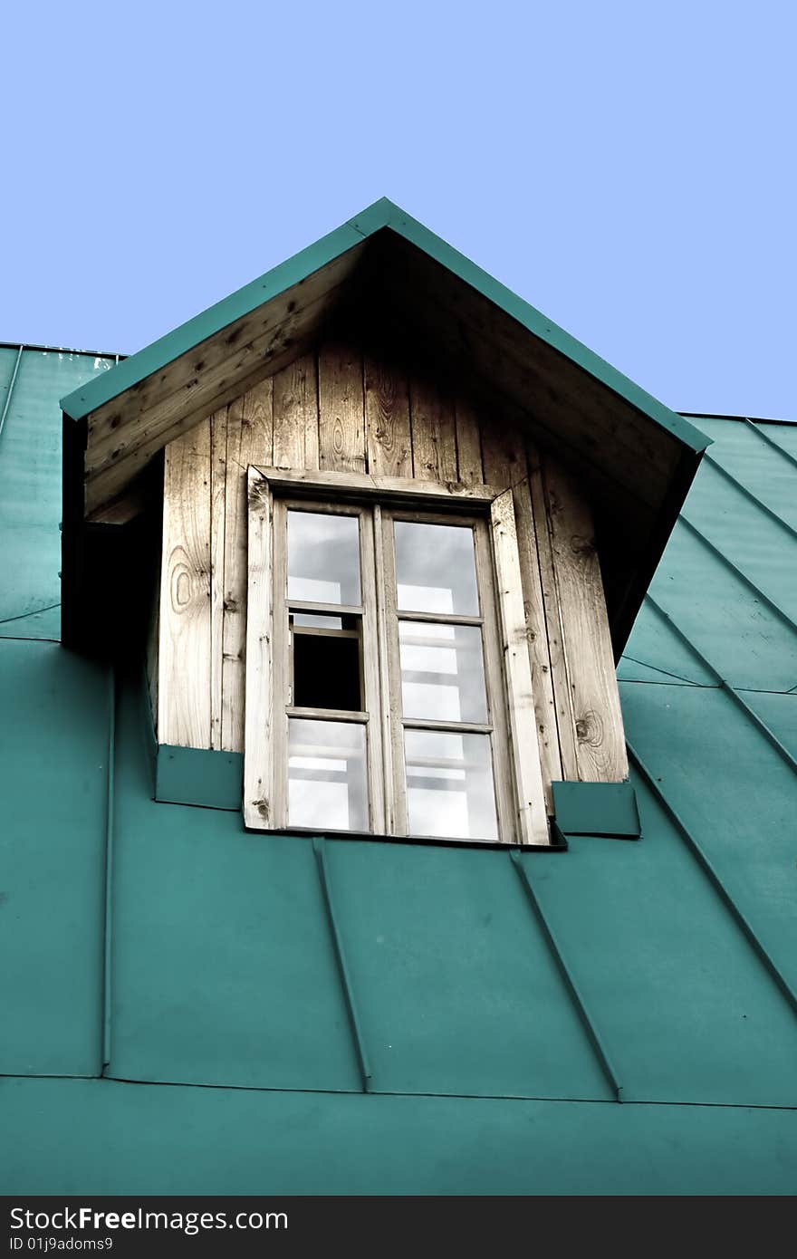 A window on top of a wooden house with a green roof. A window on top of a wooden house with a green roof