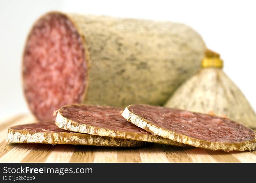 This is a piece of salami and some slices on chopping board. This is a piece of salami and some slices on chopping board.