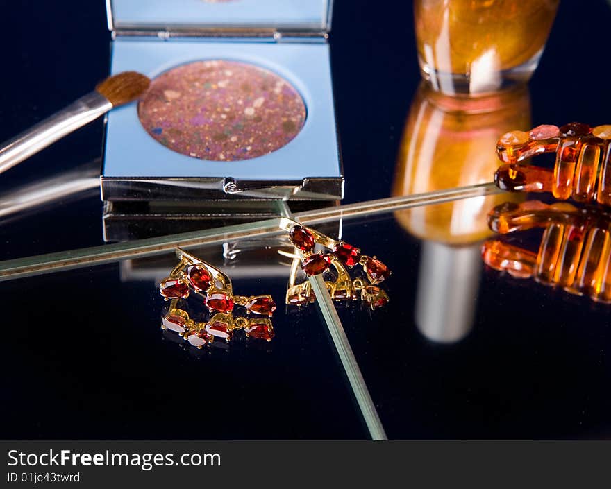 Cosmetics and golden earrings on mirror table. Cosmetics and golden earrings on mirror table