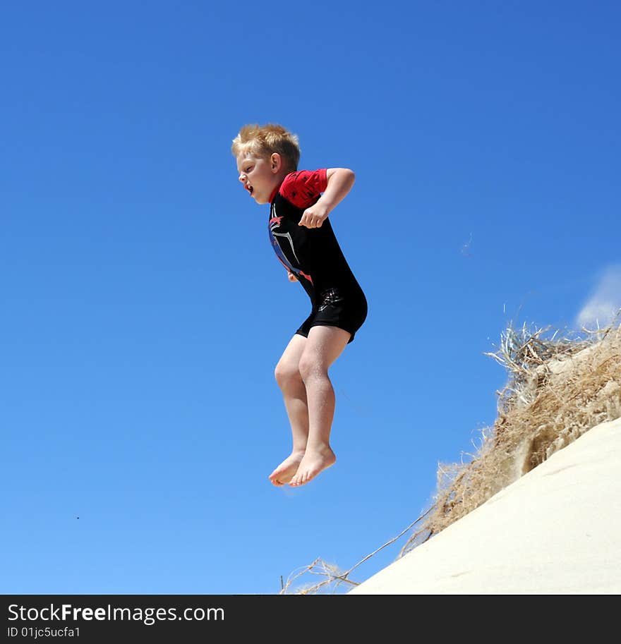 Boy jumping off sand dune